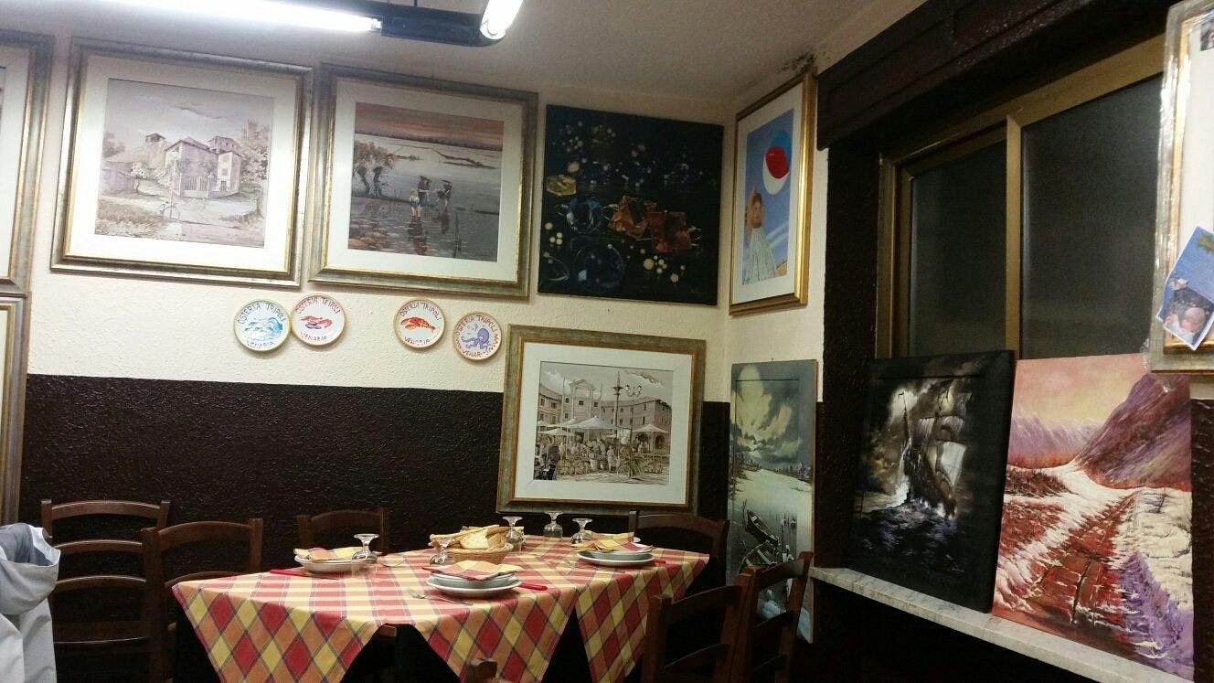 La sala dell'Osteria Tripoli: tavoli con tovaglie a quadri gialli e rossi e pareti coperte di quadri