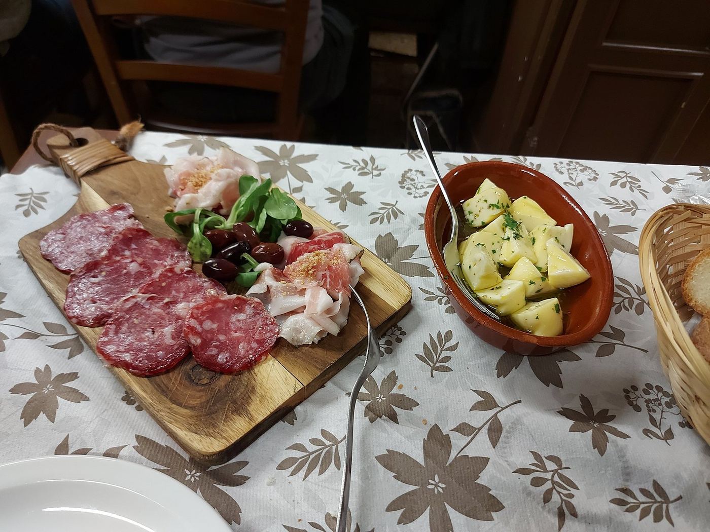 Tagliere di salumi con una ciotola di sottoli su tovaglia a fiori